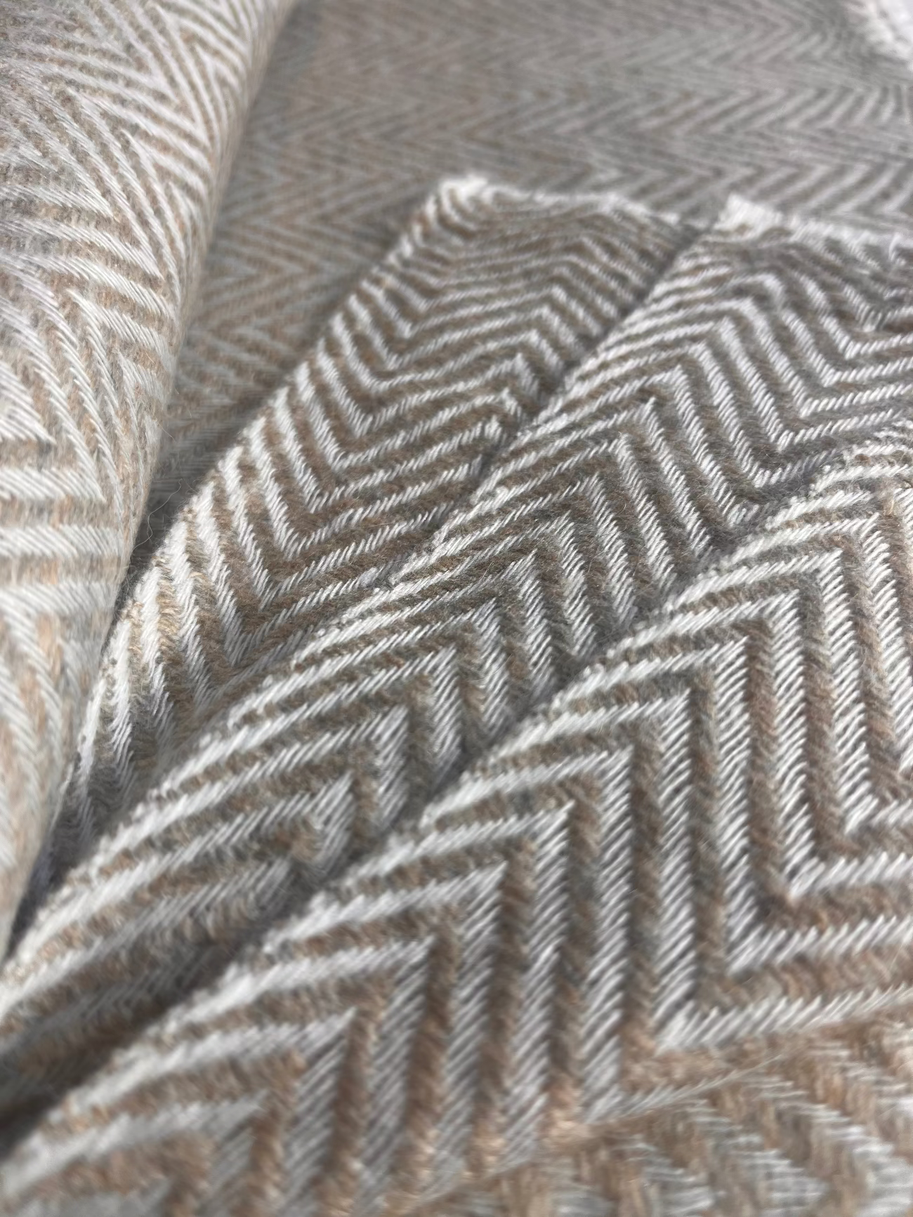 Nahaufnahme eines naturfarbenen Kamelhaarschals mit feinem Fischgrätmuster in warmen Beige- und Cremetönen. Die weiche, flauschige Textur lässt die Hochwertigkeit der handgewebten Naturfaser erkennen – stilvoll, nachhaltig und perfekt für achtsame Momente mit Stil.