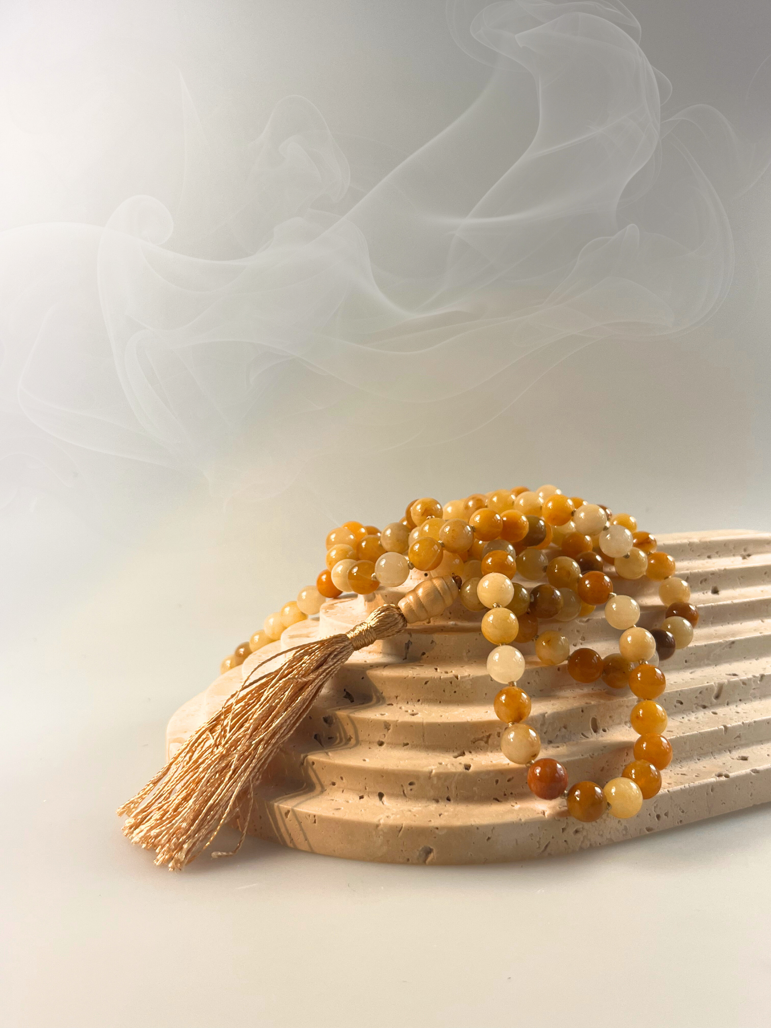 Eine handgeknüpfte Mala-Kette aus polierten Honigcalcit-Perlen in warmen Gelb- und Goldtönen, spiralförmig gelegt und mit einer goldschimmernden Quaste sowie einer glatten Guru-Perle aus hellem Holz veredelt. Das Schmuckstück ist freigestellt auf hellem Hintergrund dargestellt und eignet sich ideal für Meditation, spirituelle Rituale oder als energetisches Accessoire mit sonniger Ausstrahlung.