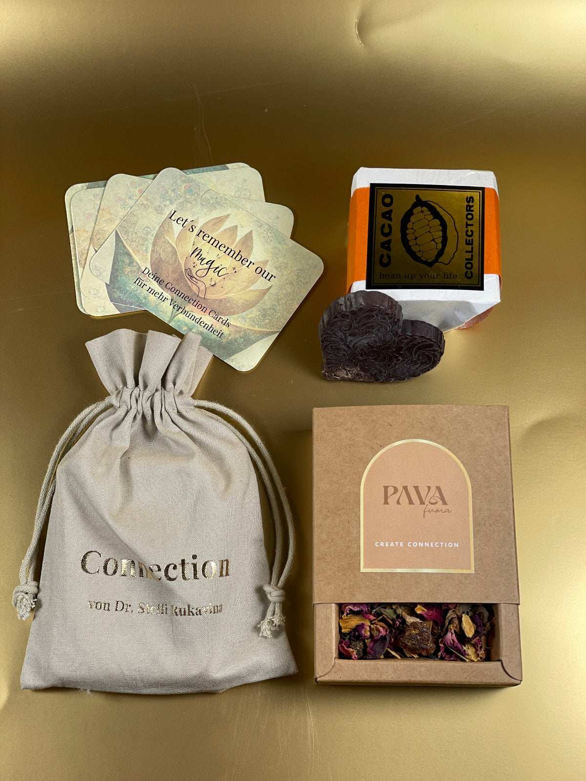 Edles Ritual-Set auf goldenem Hintergrund mit naturfarbener Stofftasche „Connection“ von Dr. Steffi Lukacova, handverlesenem Kakao-Herz, nachhaltiger PAVA FUMA Räuchermischung und liebevoll gestalteten Connection Cards – ein Geschenk der Achtsamkeit und Verbundenheit.