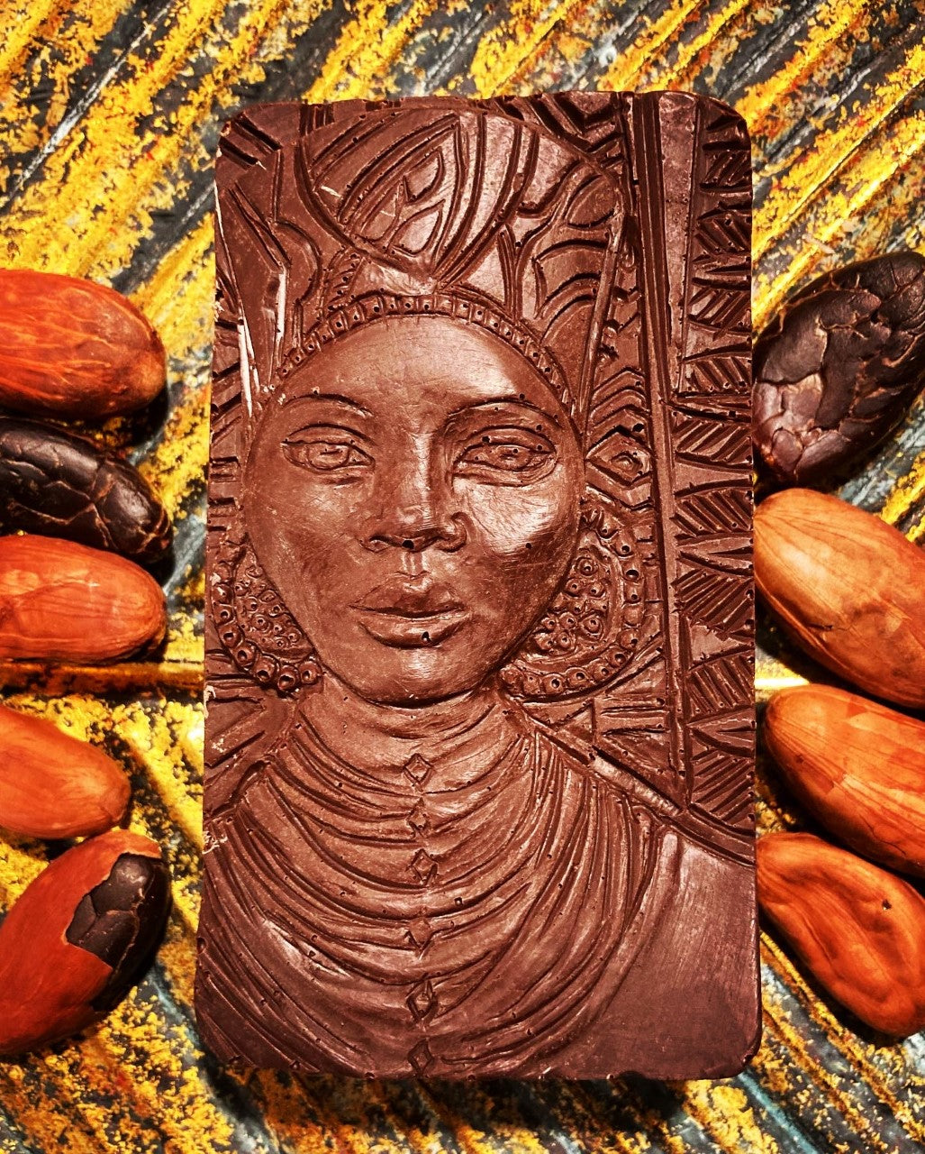 Detailreiche, handgegossene Schokoladenplatte mit kunstvoller Darstellung einer indigenen Frau – Symbol für Mama Cacao – umgeben von rohen Kakaobohnen auf natürlichem Untergrund. Ausdruck von Weiblichkeit, Ursprung und zeremoniellem Genuss.