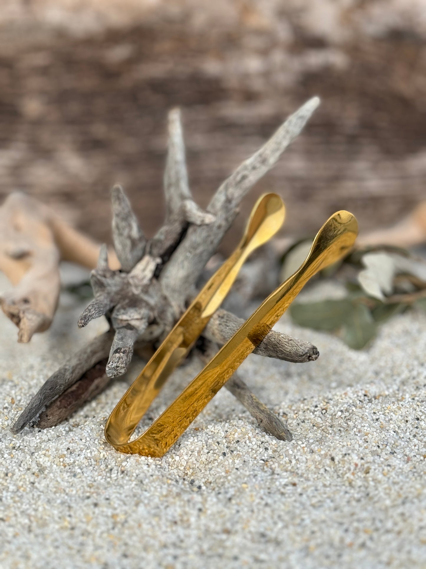 Räucherzange in gold auf einem Sandbett an ein Treibholz angelehnt