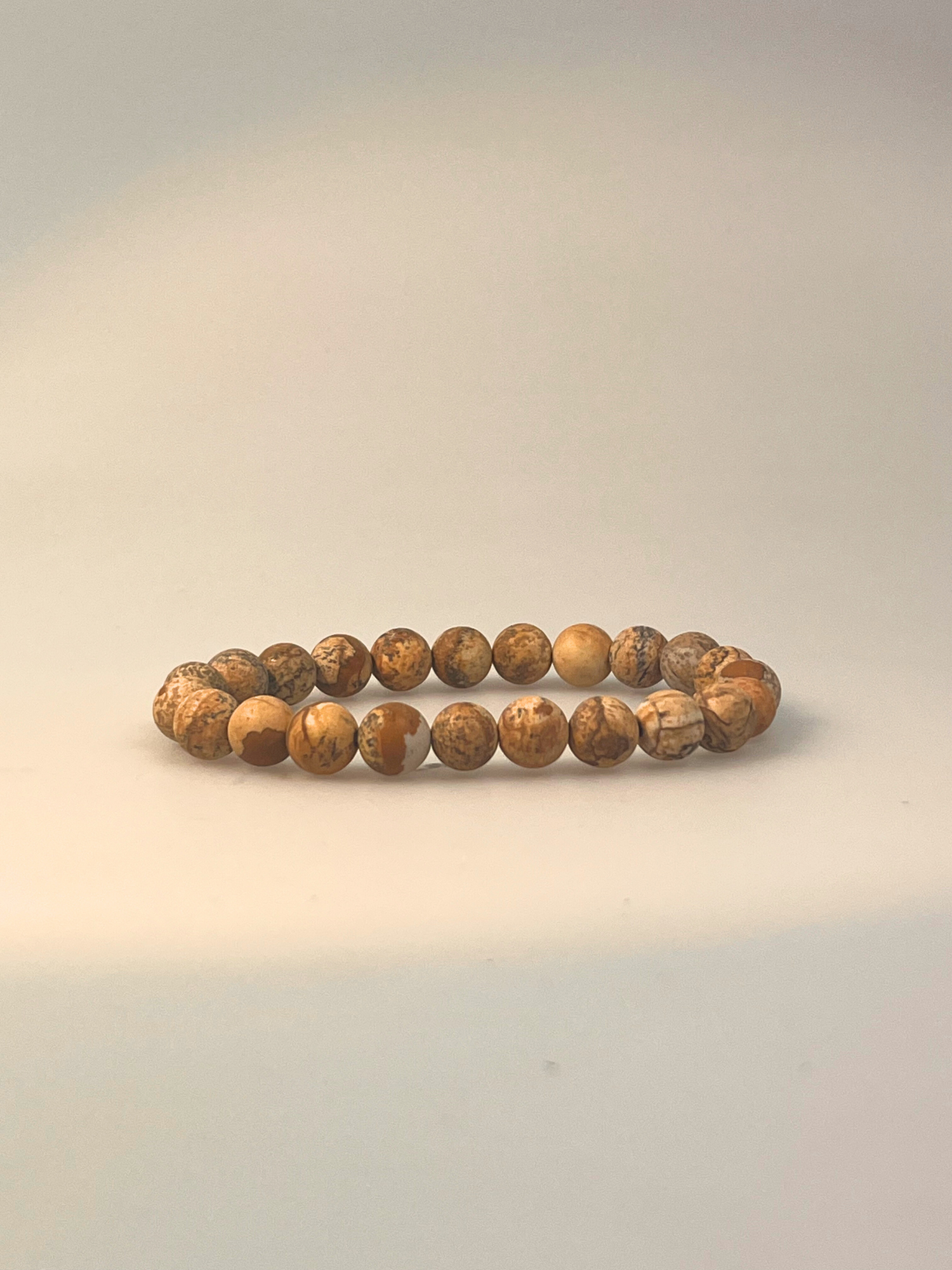 Ein elastisches Armband aus Landschaftsjaspis mit matten, runden Perlen in warmen Erd- und Beigetönen. Jede Perle zeigt eine einzigartige Maserung mit natürlichen Linien und Mustern – von sandfarben bis ockerbraun. Das Armband liegt freigestellt vor hellem Hintergrund und vermittelt eine naturnahe, erdende Ausstrahlung – ideal für Achtsamkeit, Erdung und stilvolle Begleitung im Alltag.