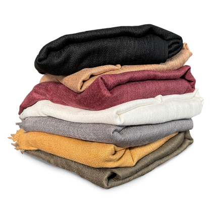 Freigestellter Stapel hochwertiger Pashmina-Schals aus Kaschmir und Seide in verschiedenen Farben – von Schwarz über Goldgelb, Burgunderrot und Cremeweiß bis hin zu Olivgrün. Die fein gewebten Schals wirken weich, edel und anschmiegsam – ideal für stilvolle Layer-Looks, als Meditations- oder Zeremonientuch oder zum Verschenken.