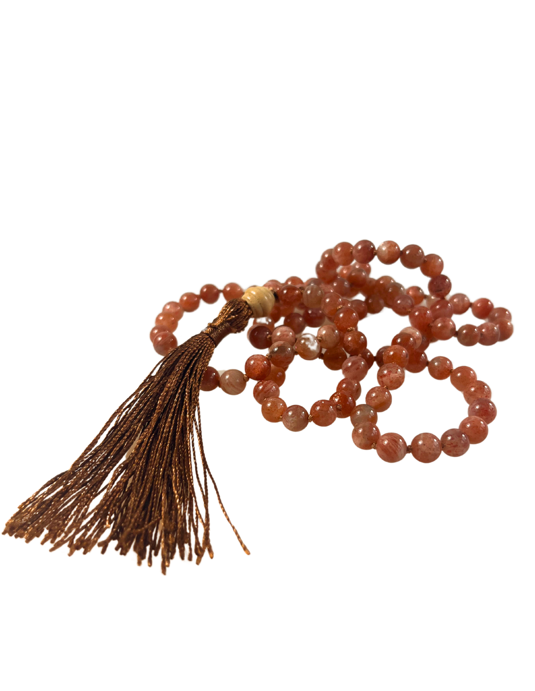 Handgeknüpfte Mala-Kette aus Sonnenstein-Perlen in warmen Kupfer- und Rosétönen, arrangiert in weicher Schlaufenform. Die Kette ist mit einer schimmernden dunkelgoldenen Quaste und einer hellen Holz-Guru-Perle veredelt. Das Schmuckstück ist freigestellt vor transparentem Hintergrund dargestellt und eignet sich ideal für energetisierende Rituale, Meditation und als stilvolles Accessoire.